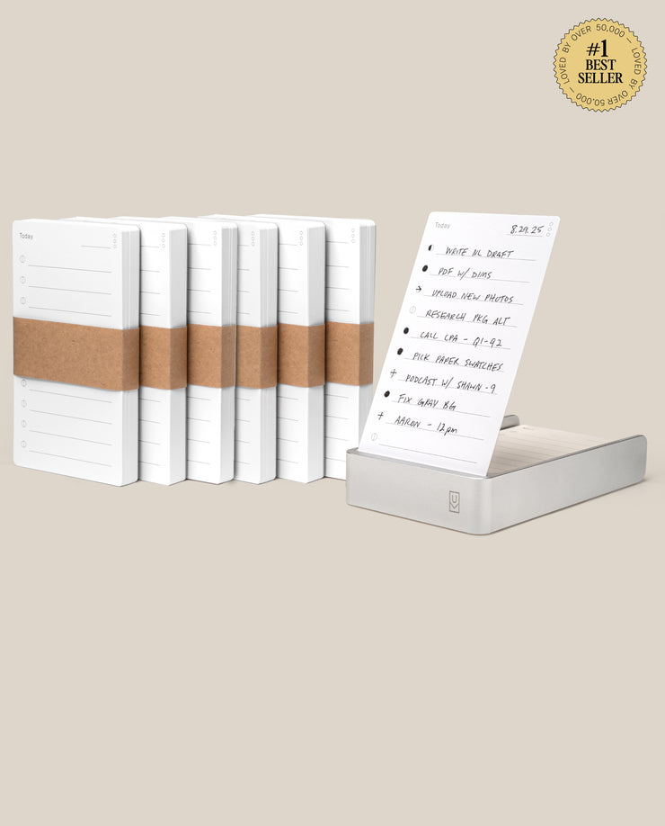 The Analog Daily Focus Kit + 6 Refills (Silver Aluminum) features a stack of six notepads wrapped in brown paper beside a single displayed notepad with a handwritten to-do list and a #1 Best Seller badge on a beige background.