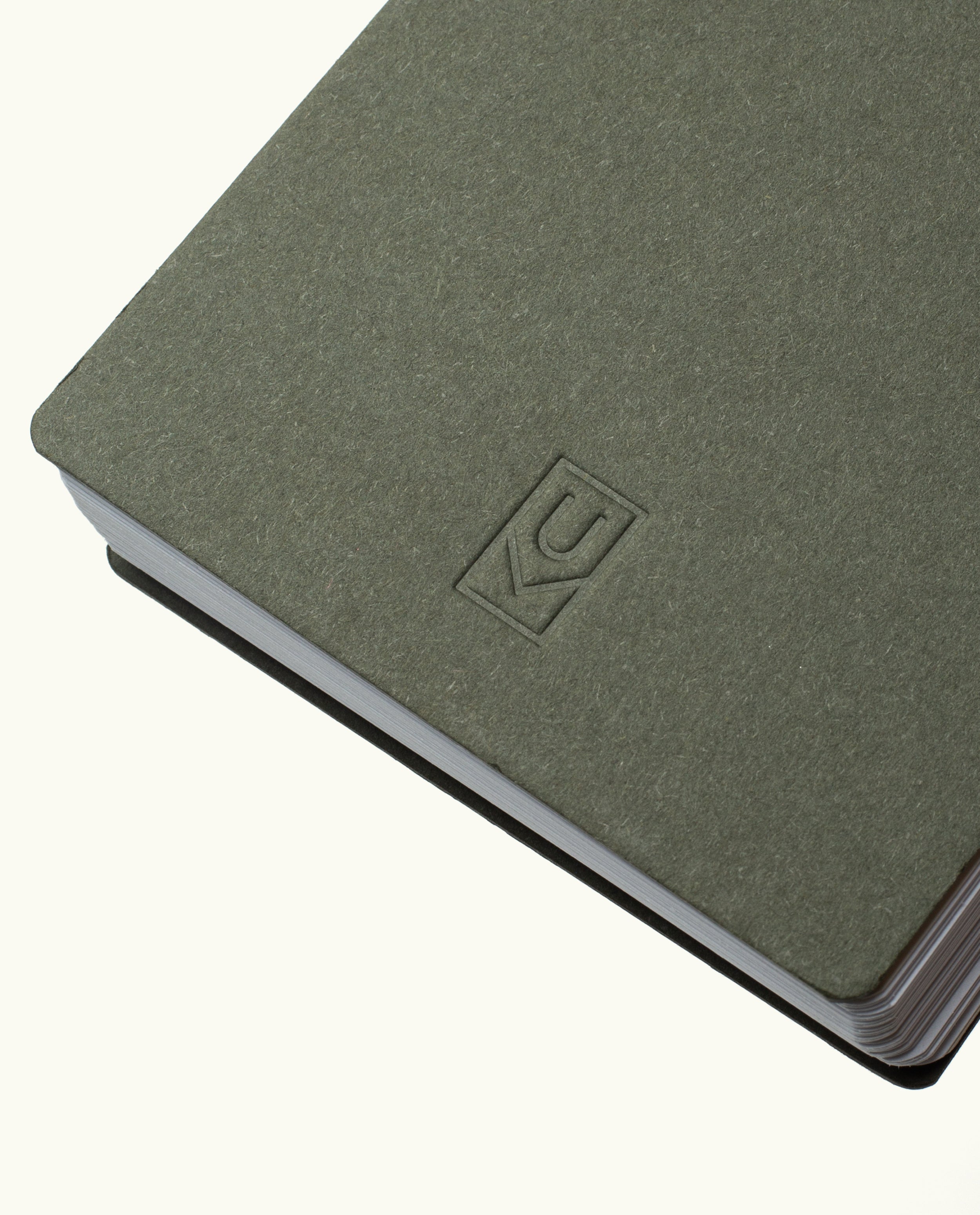 A close-up of the Discbound Analog + 3 Refills notebook in gray-green, featuring a simple embossed KC logo, brass disc binding, rounded corners, and slightly fanned pages against a plain background.
