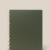 A large (8.5" x 11") Discbound Journal with a green plain cover and gold rings, refillable and spiral-bound, shown on a light beige background.