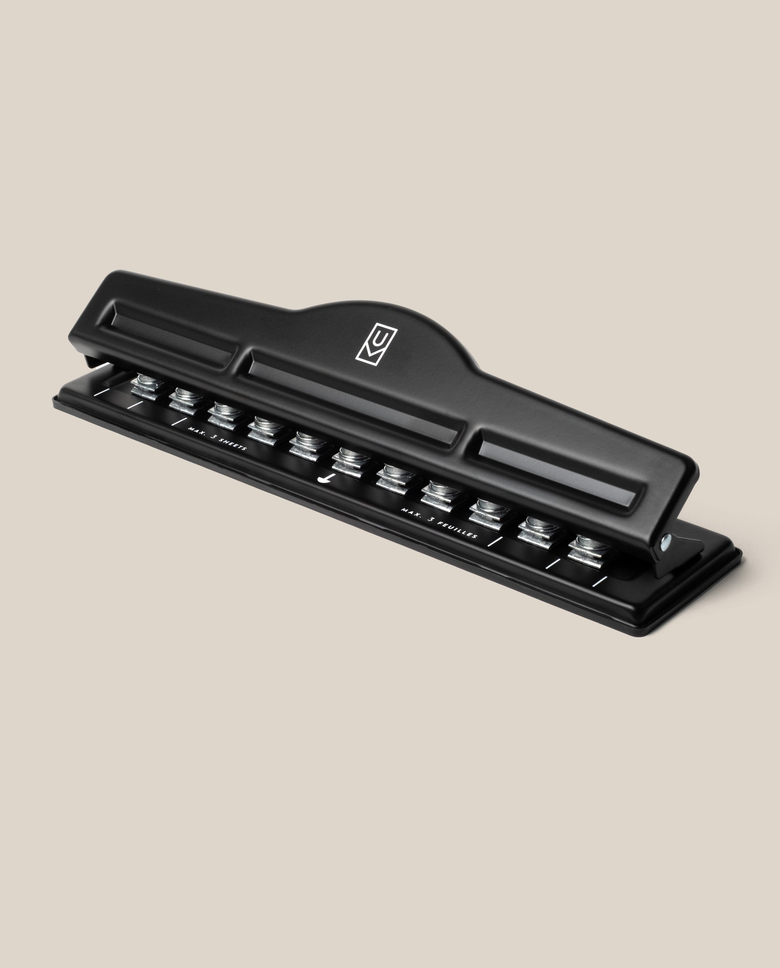 A black metal Discbound Punch with a lever handle sits at an angle on a neutral beige background—ideal for prepping pages for your Discbound Punch or any discbound system.