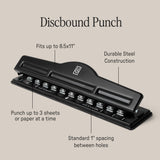 A black Discbound Punch on a beige background with labeled features: fits up to 8.5x11" paper, durable steel, punches 3 sheets at once, and standard 1" spacing—perfect for any discbound system or Ugmonk Discbound Journal.