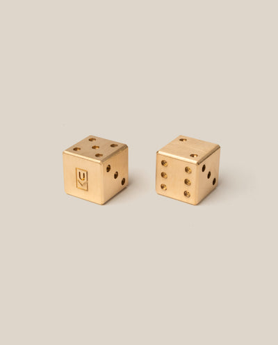 Two gold dice with U monogram on a beige background