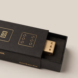Gold dice in a black box with 'MANK' branding on a beige background