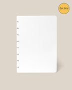 A white Discbound Journal Refill - Dot Grid (Standard 6″ x 8.5″) sheet featuring six disc-bound holes on the left is displayed against a beige background. In the top right corner, a yellow circle labeled “Dot Grid” highlights this as the ideal refill pack for your Heirloom Discbound Journal.