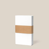 A pack of Analog Dot Grid Cards - Small (1-Pack) is bound with a brown paper band and stands upright against a beige background, ideal for analog note taking.
