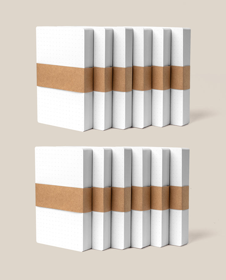 Twelve packs of Analog Dot Grid Cards - Small, neatly stacked with brown paper bands, are displayed on a beige background—ideal for organizing your notes with a total of 600 compact index cards.