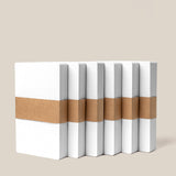 Six Analog Dot Grid Cards - Small (6-Pack), each with a white dotted cover and brown kraft paper band, stand upright in a row against a beige background—ideal for note taking or pairing with other dot grid cards.