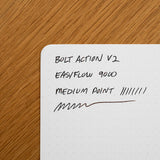 A dotted notebook page on wood with handwritten notes: INVENTERY Bolt Action Pen (Stainless), EASYFLOW 9000, MEDIUM POINT, pen test lines—showing the smooth performance of this Los Angeles-made pen.