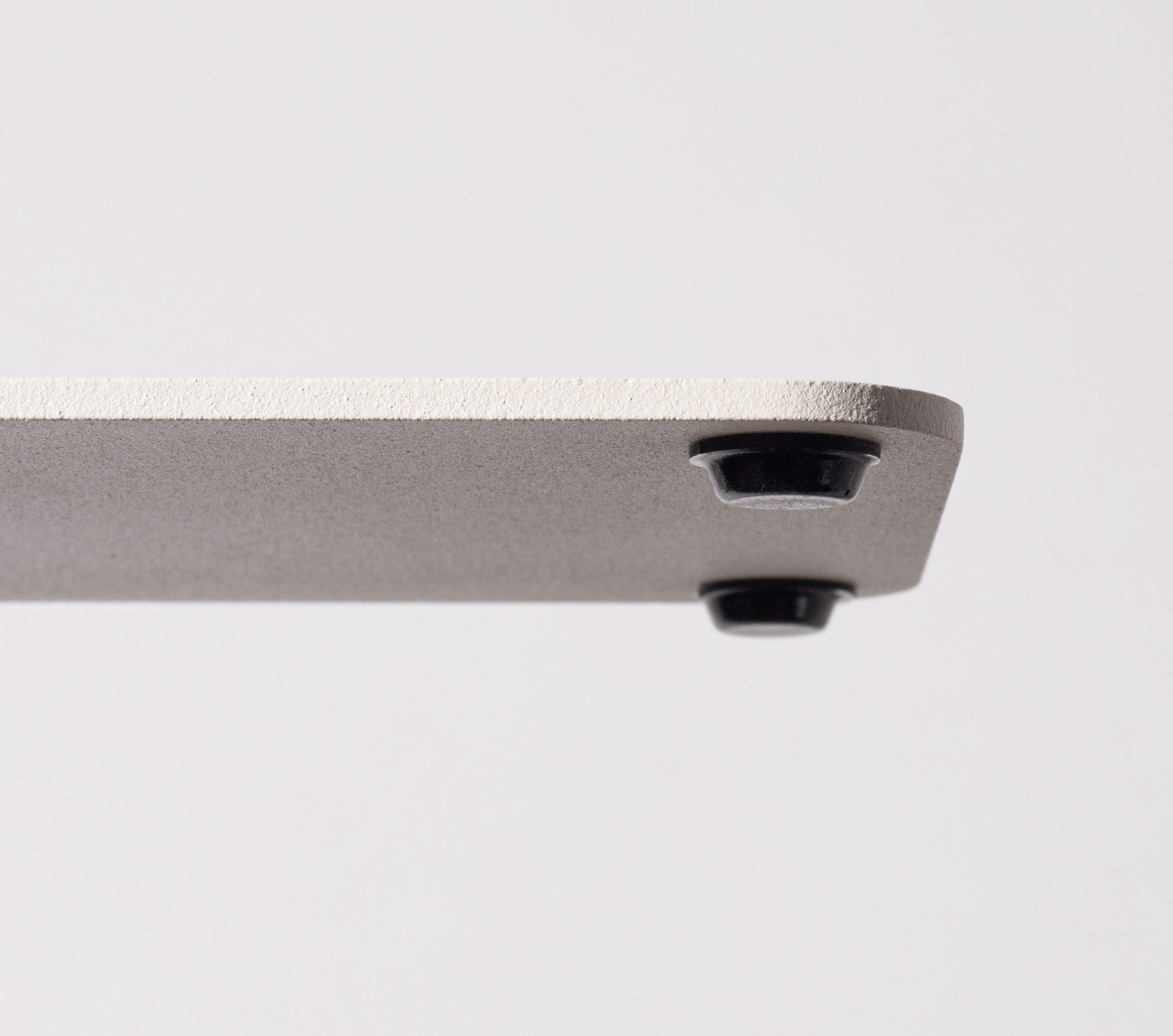A close-up of the corner of a white Gather 2x2 Base Plate shows two small black cylindrical feet underneath. Made from powder coated steel, it rests on a plain white background.