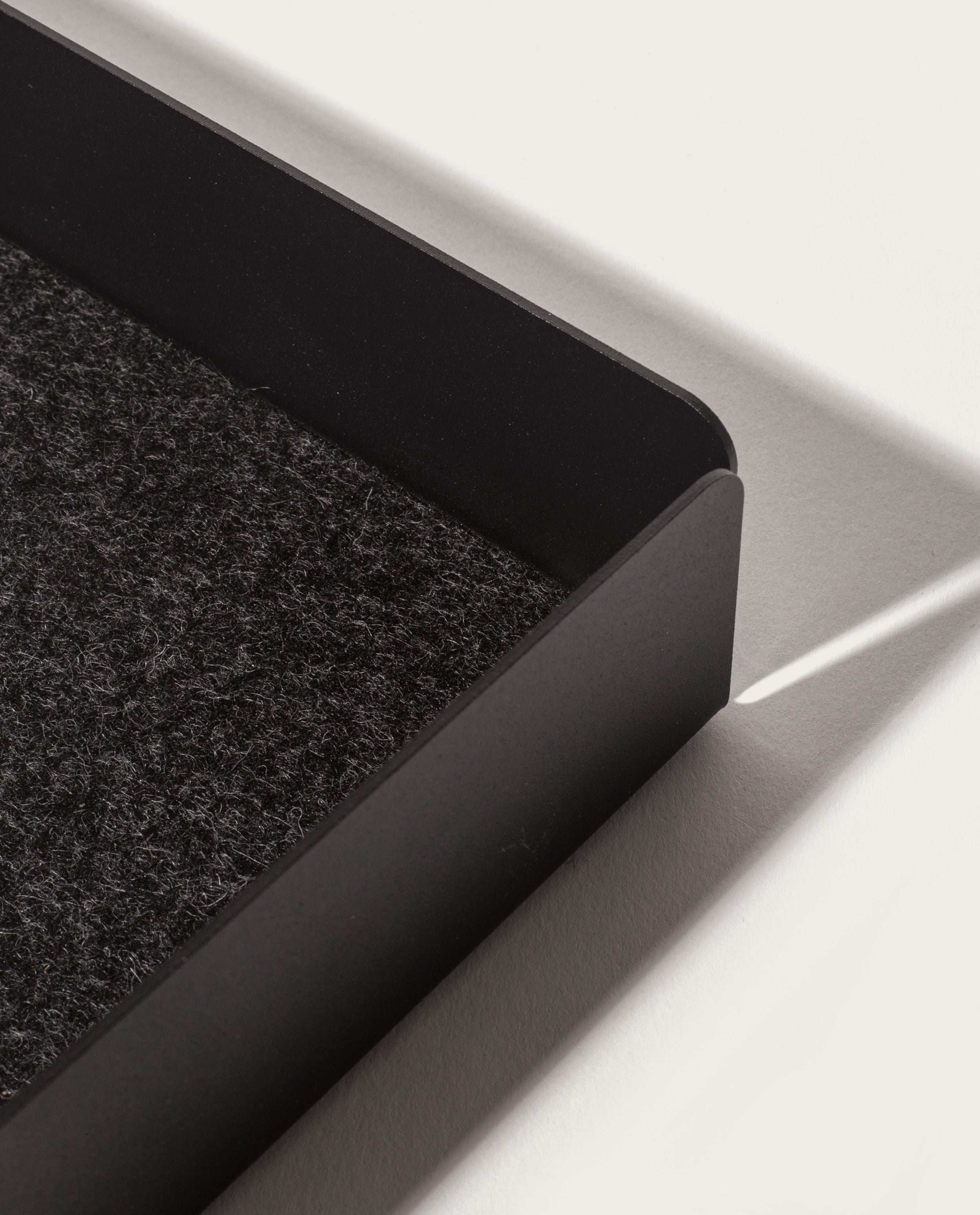 A close-up of the Gather Large Tray (2x2 - Black) featuring a textured dark felt interior and magnetic base, casting a shadow on a white surface in bright light.