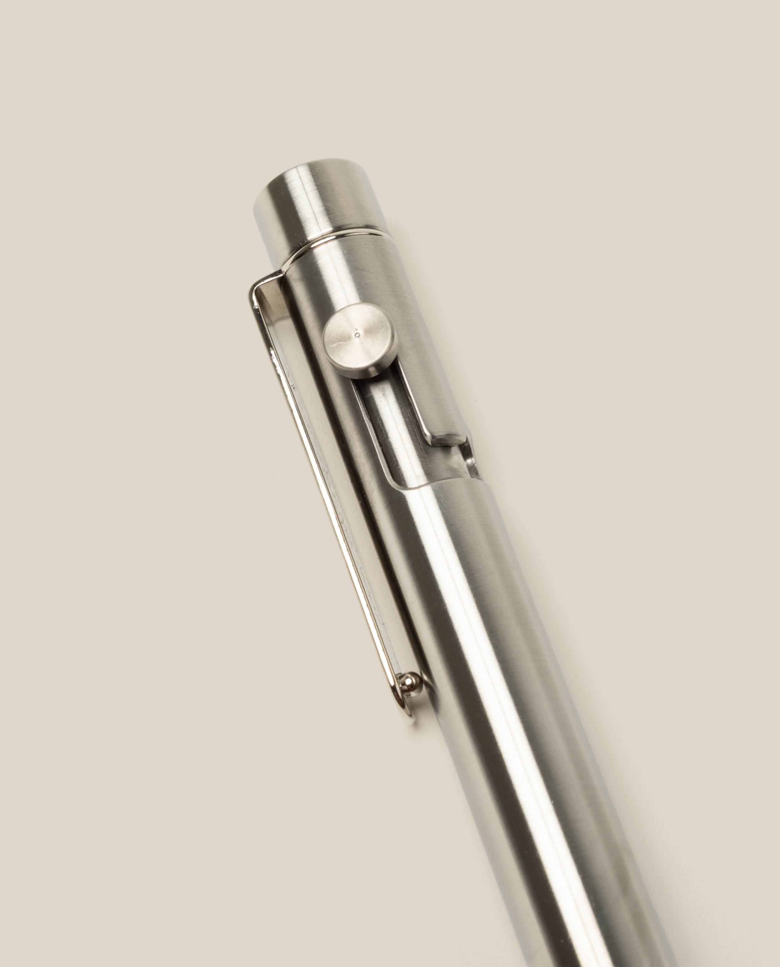 A close-up of the INVENTERY Bolt Action Pen (Stainless) with a clip, highlighting its sleek stainless steel design against a plain, light beige background.