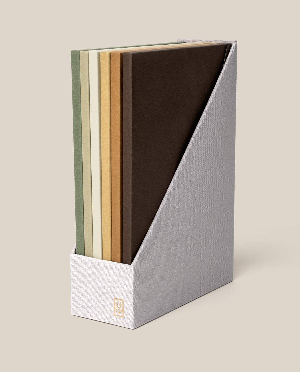Five books with earth-toned covers are neatly arranged vertically in a light gray, angled book holder against a beige background, capturing the organized charm of the Discbound Journal Archive and evoking its practical elegance.