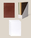 The Discbound Heirloom Journal Bundle, featuring a brown leather 6″ x 8.5″ refillable journal and three paper refills, is displayed on a beige background.