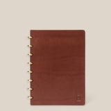 The Discbound Heirloom Journal (Brown Leather, 6" x 8.5") features refillable pages, gold disc binding, and a subtle embossed logo in the bottom right corner, shown on a plain beige background.