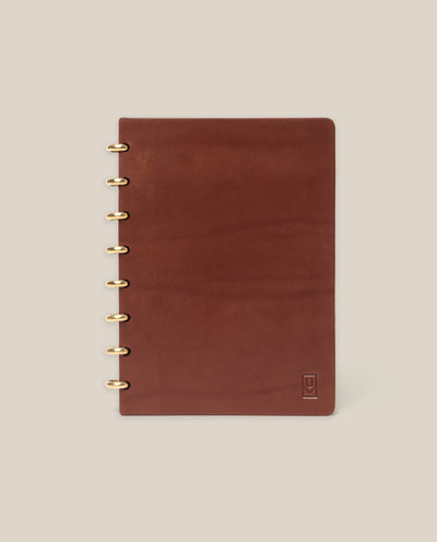 The Discbound Heirloom Journal (Brown Leather, 6" x 8.5") features refillable pages, gold disc binding, and a subtle embossed logo in the bottom right corner, shown on a plain beige background.