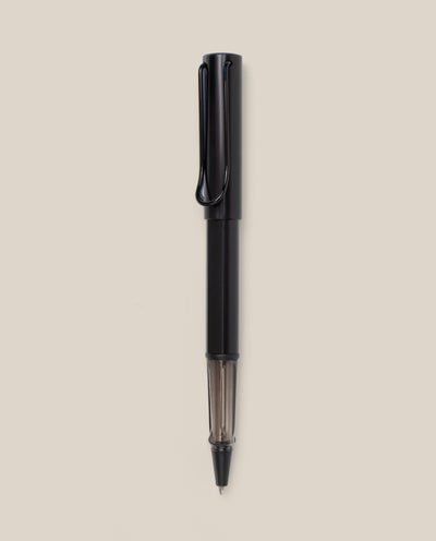 A black LAMY AL-star Rollerball pen with a transparent section near the tip is vertically centered on a plain beige background, highlighting its smooth writing experience and refillable rollerball design.