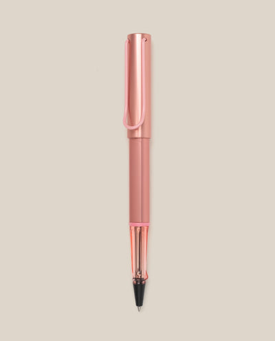 The LAMY AL-star Rollerball (Flamingo) features a pink anodized aluminum body, clear grip, and black ink tip, shown vertically on a light beige background for smooth writing.