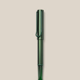 A LAMY AL-star Rollerball (Pine) pen in green metallic, with matching cap and clip, is displayed vertically on a plain light beige background. This refillable pen ensures smooth, effortless writing.