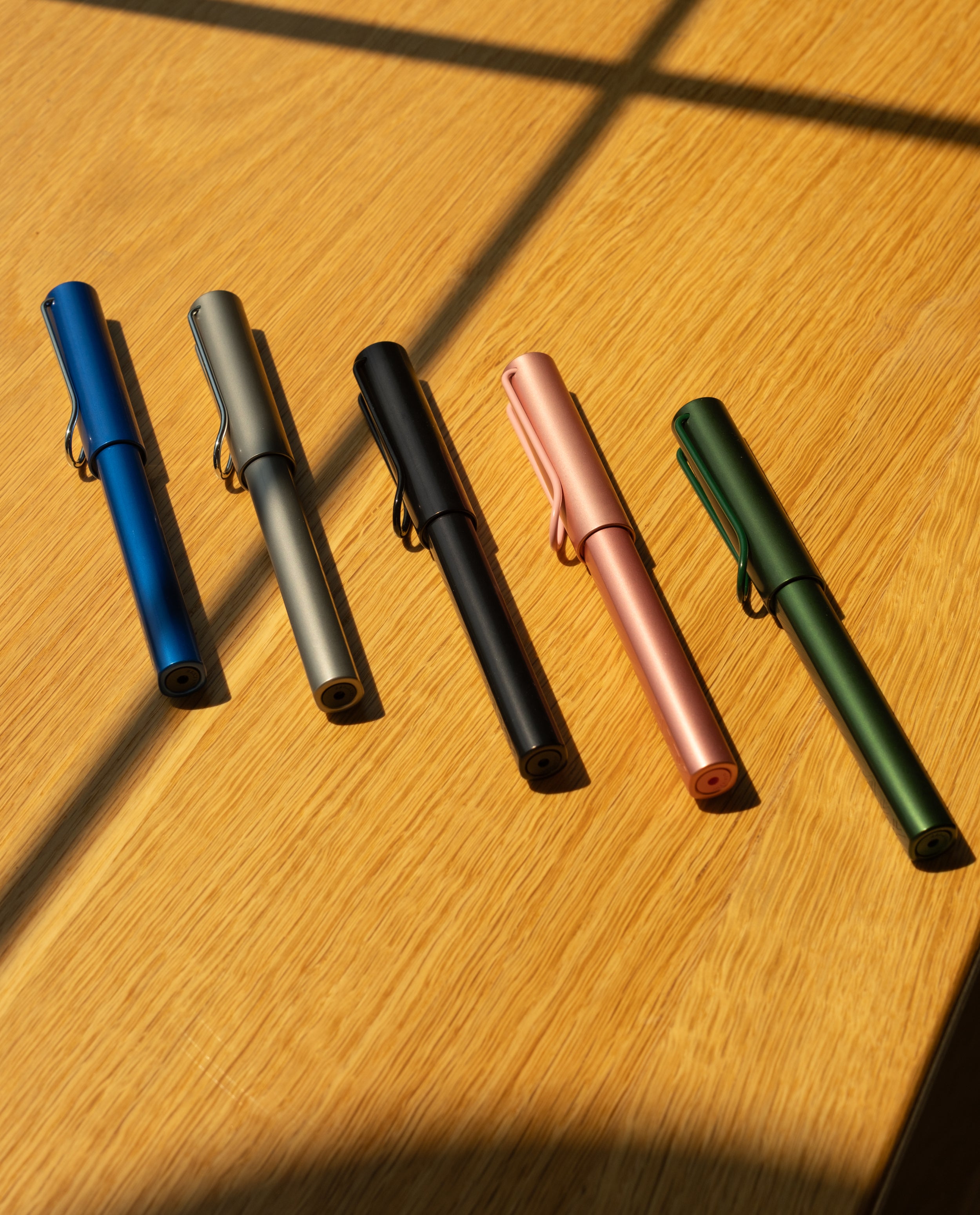 A LAMY AL-star Rollerball (Graphite) is displayed on a wooden surface with sunlight and shadows, highlighting its smooth writing performance and refillable rollerball design.