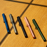 A LAMY AL-star Rollerball (Graphite) is displayed on a wooden surface with sunlight and shadows, highlighting its smooth writing performance and refillable rollerball design.