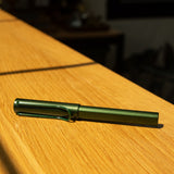 A LAMY AL-star Rollerball (Pine) rests on a sunlit wooden surface, casting a rightward shadow—a refillable rollerball pen recognized for its smooth writing experience.