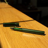 A LAMY AL-star Rollerball (Pine) with its cap off rests on a sunlit wooden surface, casting a soft shadow—ready to deliver smooth writing whenever inspiration strikes.