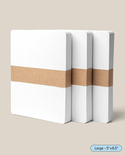 Three Analog Dot Grid Cards - Large (3-Pack), featuring white, square-edged covers and brown paper bands, stand upright on a beige background. Made from premium card stock, they're perfect for note taking. A corner label reads "Large - 5” x 6.5”.