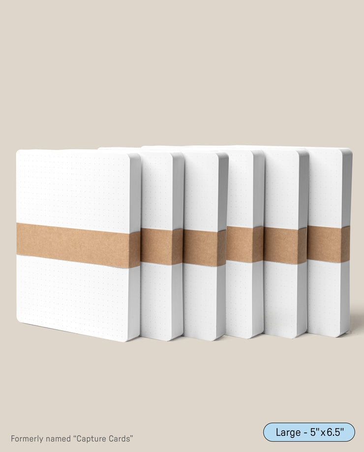 Six stacks of Analog Dot Grid Cards - Large (6-Pack), made from premium card stock, stand upright with brown paper bands. The cards are 5 x 6.5 inches for note taking and were formerly called Capture Cards.