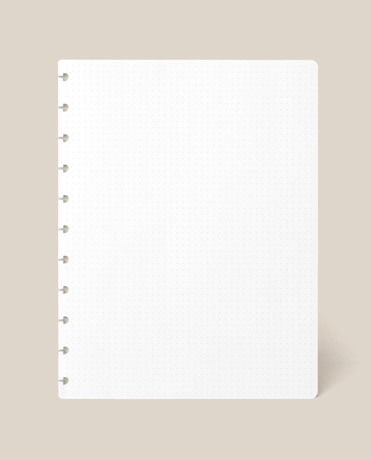 A Large Discbound Journal Refill - Dot Grid (8.5″ x 11″) sheet, featuring a square white page with round discbound holes along the left edge, is displayed against a light beige background.