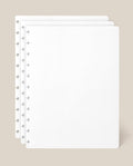 Three sheets of the Large Discbound Journal Refill - Dot Grid (8.5″ x 11″)—white and perforated—are stacked with offset edges on a beige background, making them ideal for expanding your discbound notebook.