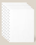 Six stacked sheets of Large Discbound Journal Refill - Dot Grid (8.5″ x 11″) rest on a beige background, aligned to display the edge holes and subtle dot grid pattern. The sheets are clean, empty, and slightly overlapping.