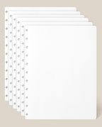 Six stacked sheets of Large Discbound Journal Refill - Dot Grid (8.5″ x 11″) rest on a beige background, aligned to display the edge holes and subtle dot grid pattern. The sheets are clean, empty, and slightly overlapping.