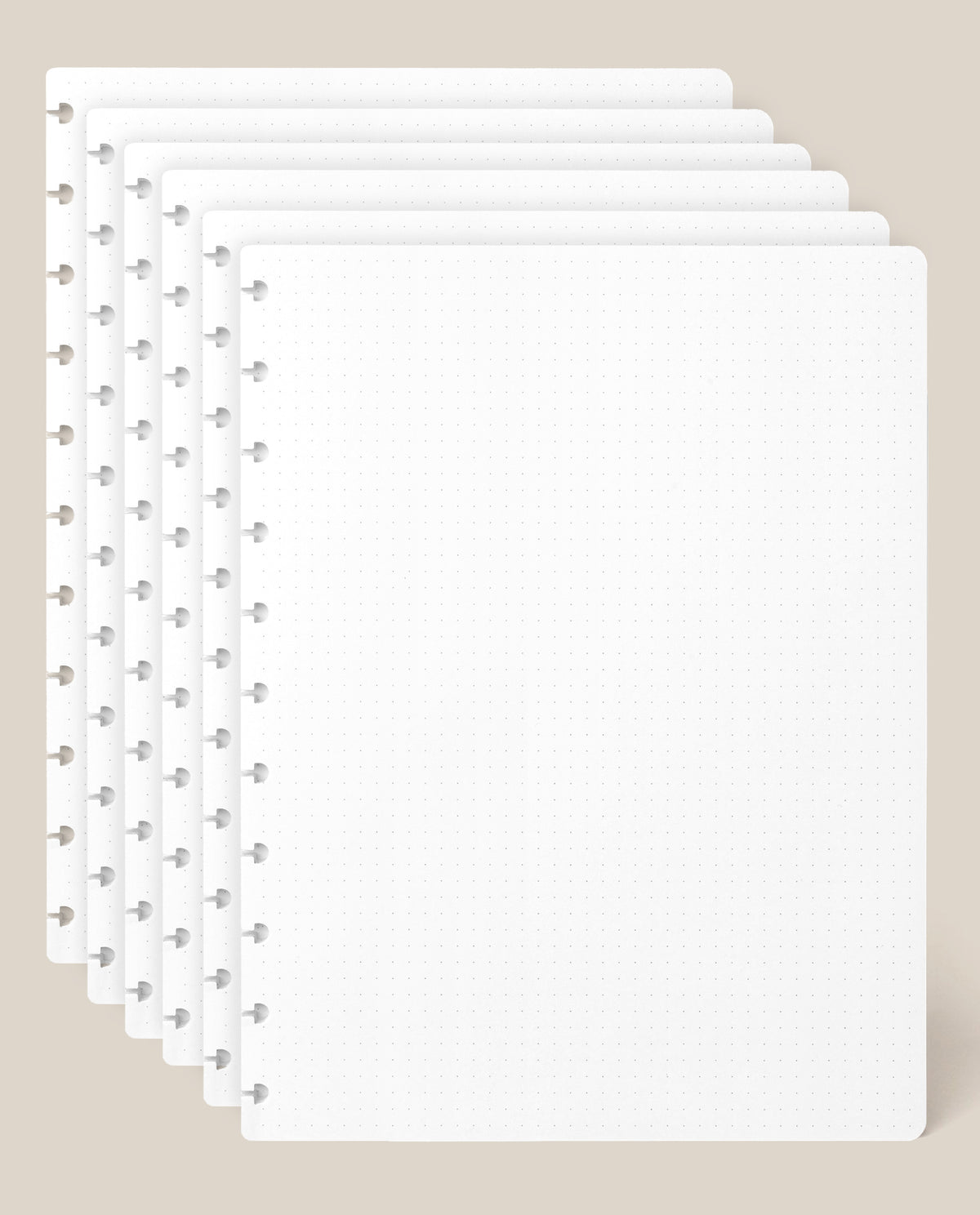 Six stacked sheets of Large Discbound Journal Refill - Dot Grid (8.5″ x 11″) rest on a beige background, aligned to display the edge holes and subtle dot grid pattern. The sheets are clean, empty, and slightly overlapping.