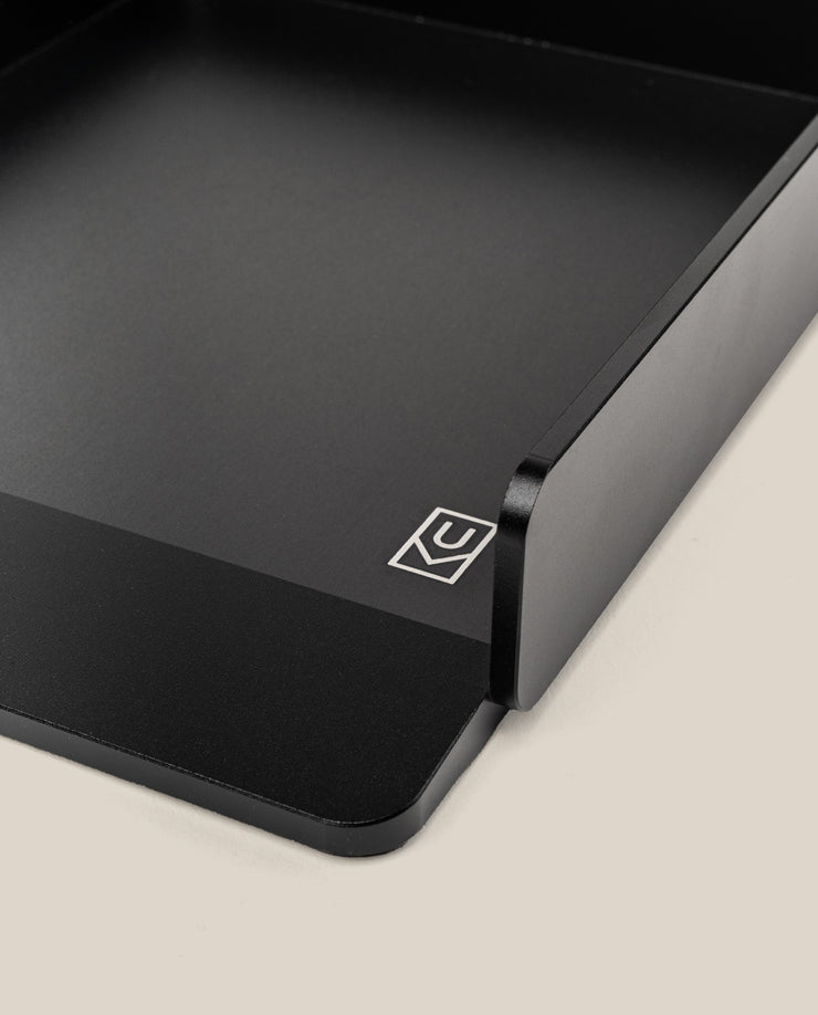 A close-up of the Analog Capture Kit - Large (Black Aluminum): a minimalist aluminum card tray with angular corners and a white geometric logo, on a light beige background—ideal for organizing large dot grid cards.