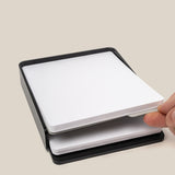 A hand places a divider card between two stacks of large dot grid cards in a black tray. Text: The Analog Capture Kit - Large (Black Aluminum) includes a divider to separate new and used cards—perfect for organizing your workflow.