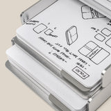 The Analog Capture Kit - 2 Large (Silver Aluminum) is displayed open, revealing dot grid notebooks and cards with black ink sketches and notes on folding and wallet designs on crisp white pages.