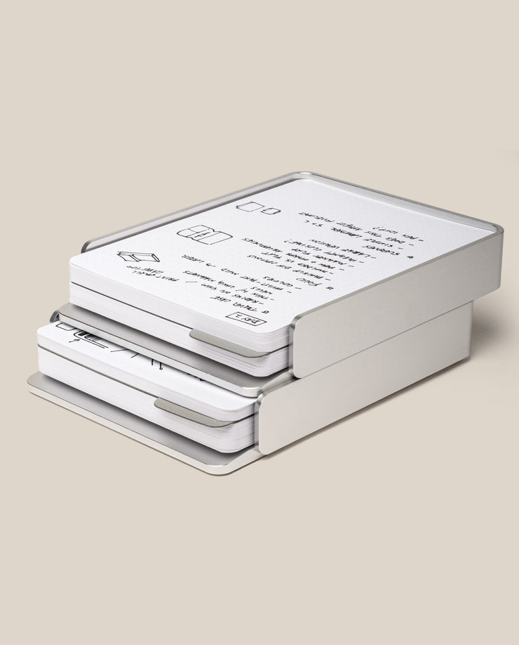 A stack of Analog Capture Kit - 2 Large (Silver Aluminum) trays holds neatly arranged paper with diagrams and text on a light beige background, showcasing a minimalist, modern design and an elegant silver aluminum card tray.