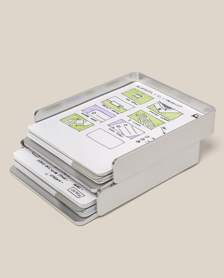 The Analog Capture Kit - 2 Large (Silver Aluminum) holds stacked dot grid cards with hand-drawn website or app wireframes, highlighting sections in green and purple, against a plain light beige background.