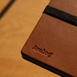 Brown leather notebook with 'Analog' branding on a wooden surface