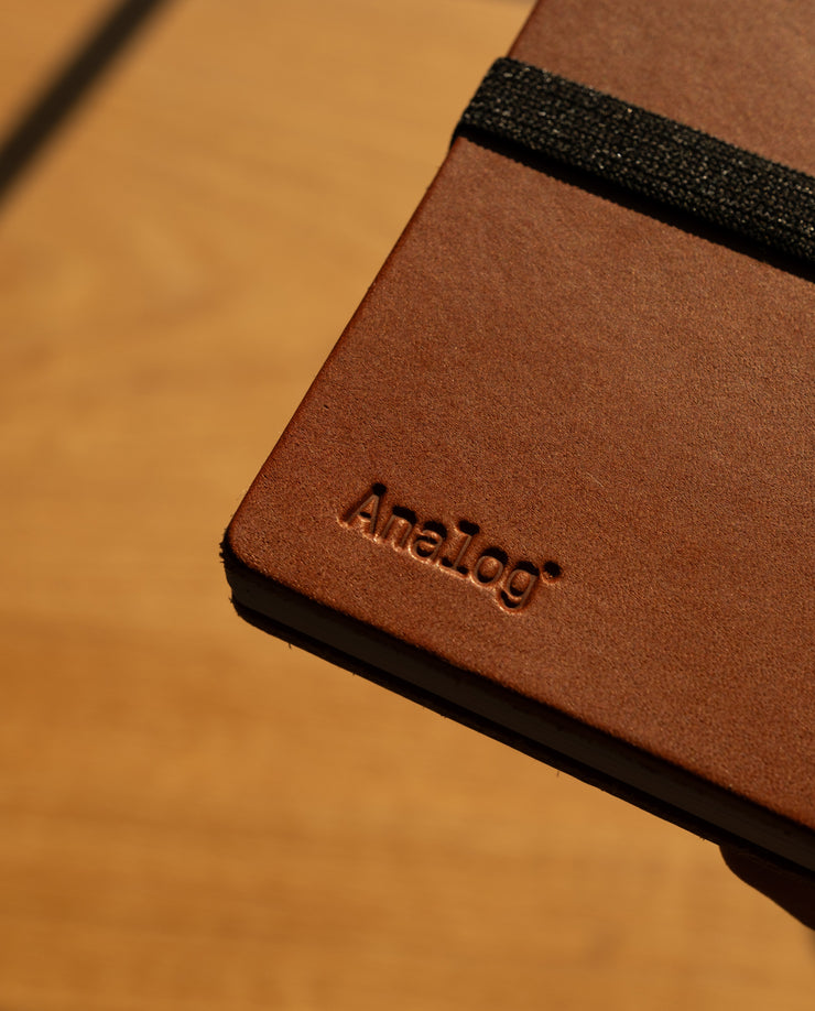 Brown leather notebook with 'Analog' branding on a wooden surface