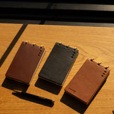 Three leather-bound notebooks in brown and black on a wooden surface.