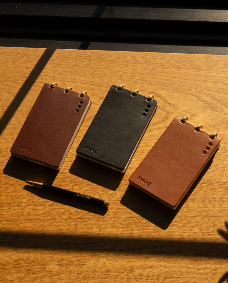 Three leather-bound notebooks in brown and black on a wooden surface.