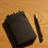 Black notebook with gold accents and a matching pen on a wooden surface