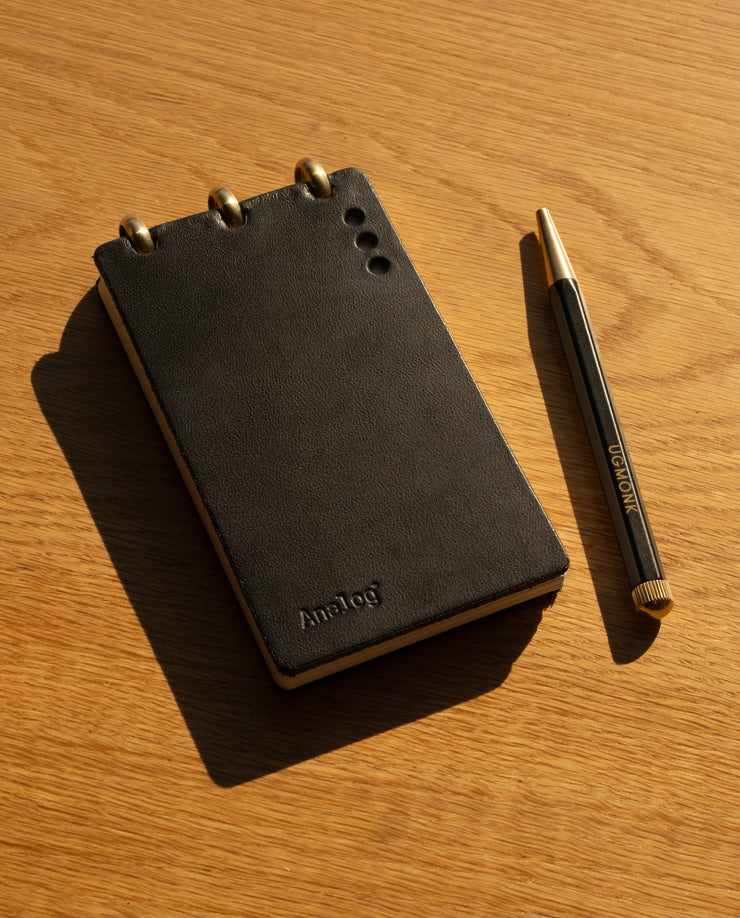Black notebook with gold accents and a matching pen on a wooden surface