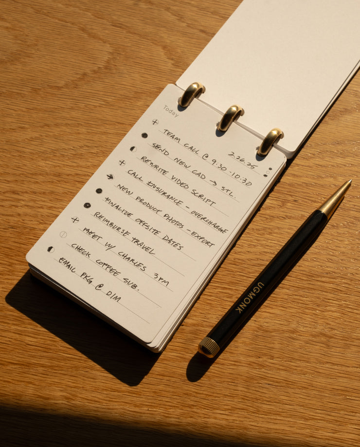 Notebook with handwritten to-do list on a wooden surface with a pen next to it