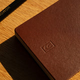 Brown leather notebook with a logo on a wooden surface