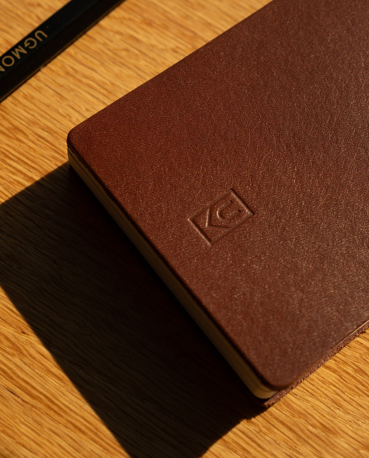 Brown leather notebook with a logo on a wooden surface