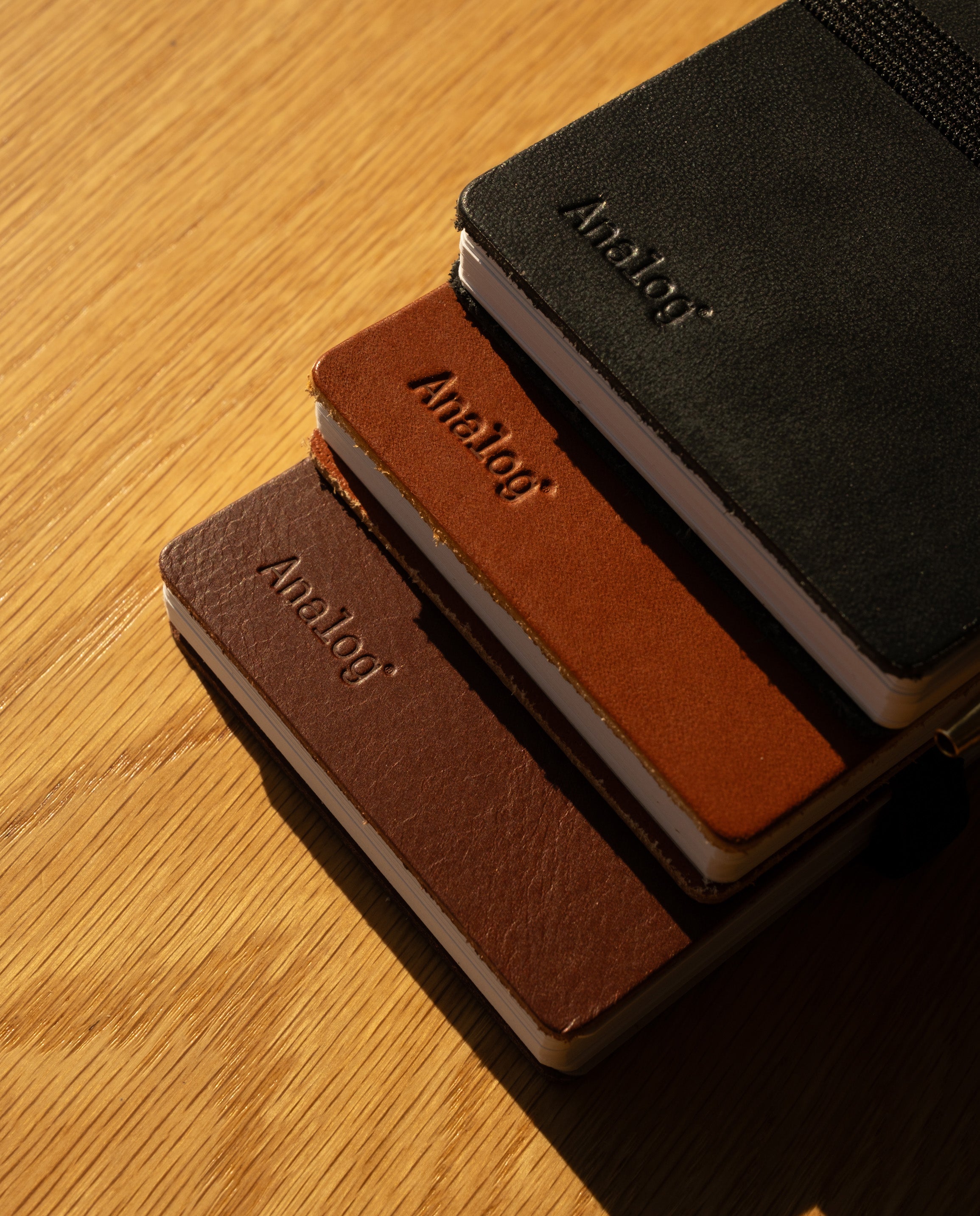 A Leather Discbound Analog + 3 Refills (Tan) notebook with a full-grain leather cover rests on a wooden surface, sunlight casting soft shadows across the scene.