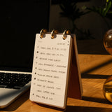 Notebook with a to-do list on a wooden desk next to a laptop