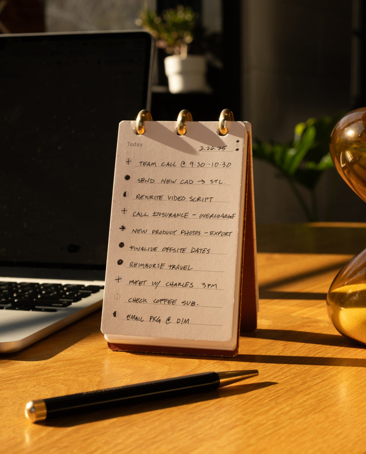 Notebook with a to-do list on a desk next to a laptop